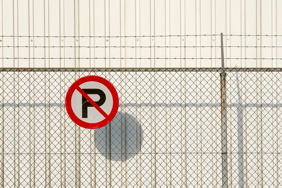 A close-up of a black and white plastic 'No Trespassing' sign with bold red letters attached to the interior of a vehicle window using white tape. The sign features a blank area below the message, pos