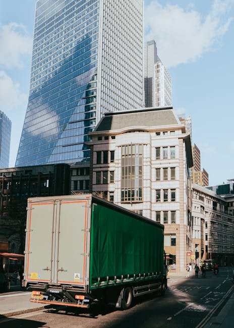 Photograph of three large pink moving containers with black lettering and contact details, positioned side by side along a paved area against a brick wall under an overcast sky. The containers appear
