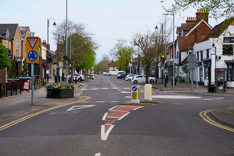 An aerial view of a busy residential street in Hounslow, featuring parked cars along the curb, a red double-decker bus in motion, and a white van, which may be used for home relocation services by com