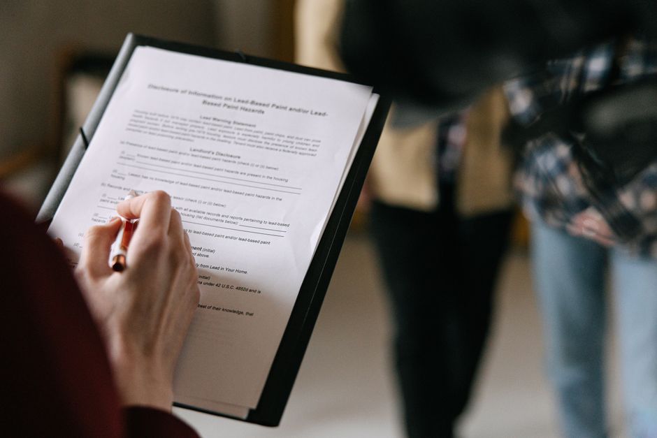 A person holding a clipboard with a typed document regarding Tenancy Notice and Moving Rules for Hounslow Landlords, using a red pen to make notes or annotations. The scene is set indoors with a blurr